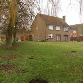 The back-garden with a view towards the back-drive to the right, and the detached garage to the left.